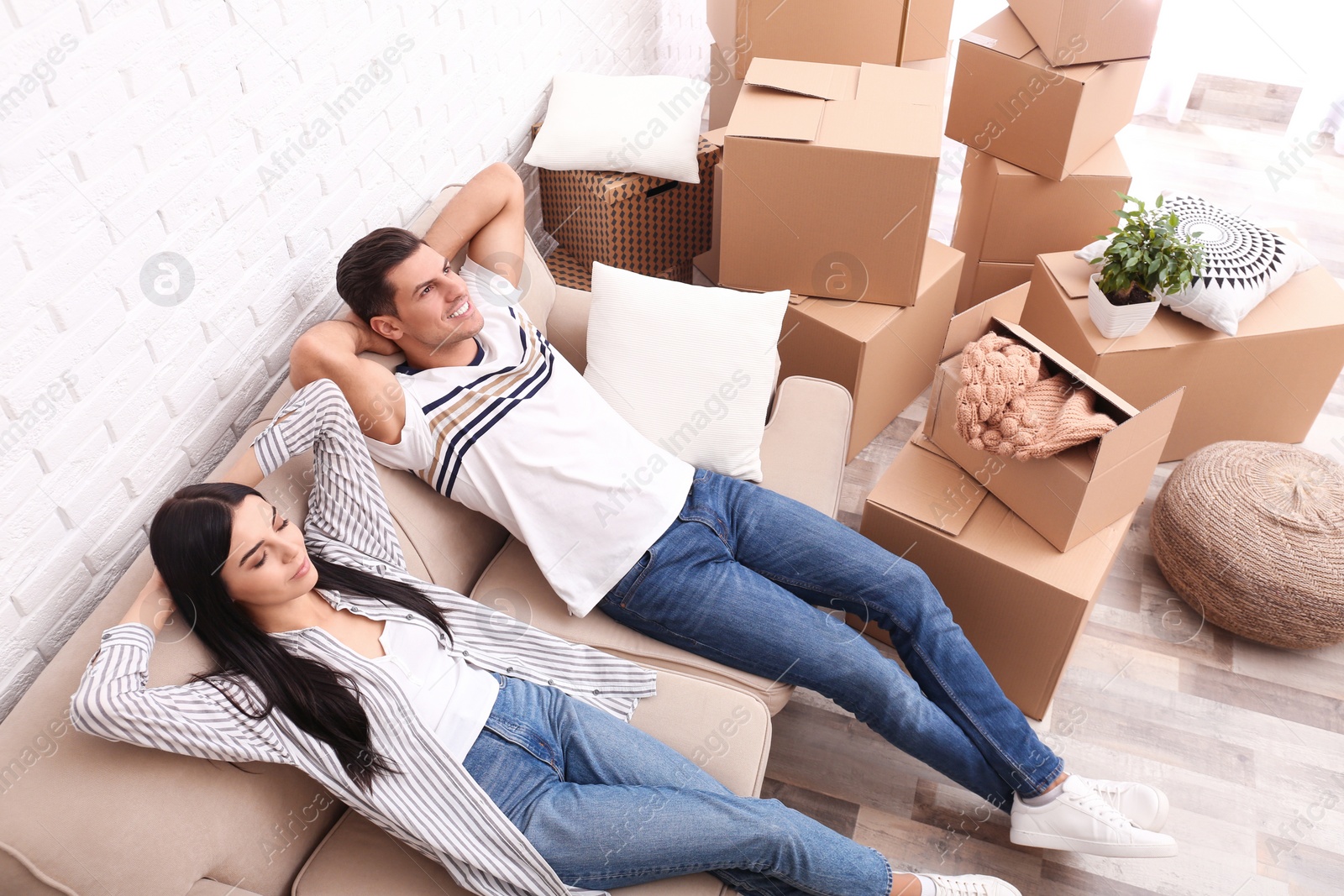 Photo of Happy couple resting in room with cardboard boxes on moving day, above view