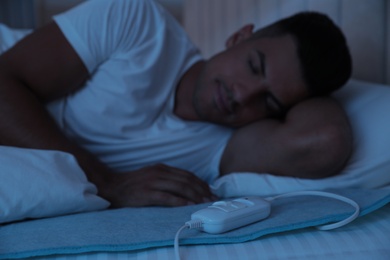 Photo of Man sleeping in bed with electric heating pad, focus on cable