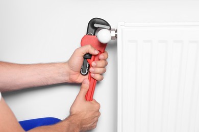 Photo of Professional plumber using adjustable wrench for installing new heating radiator near white wall, closeup