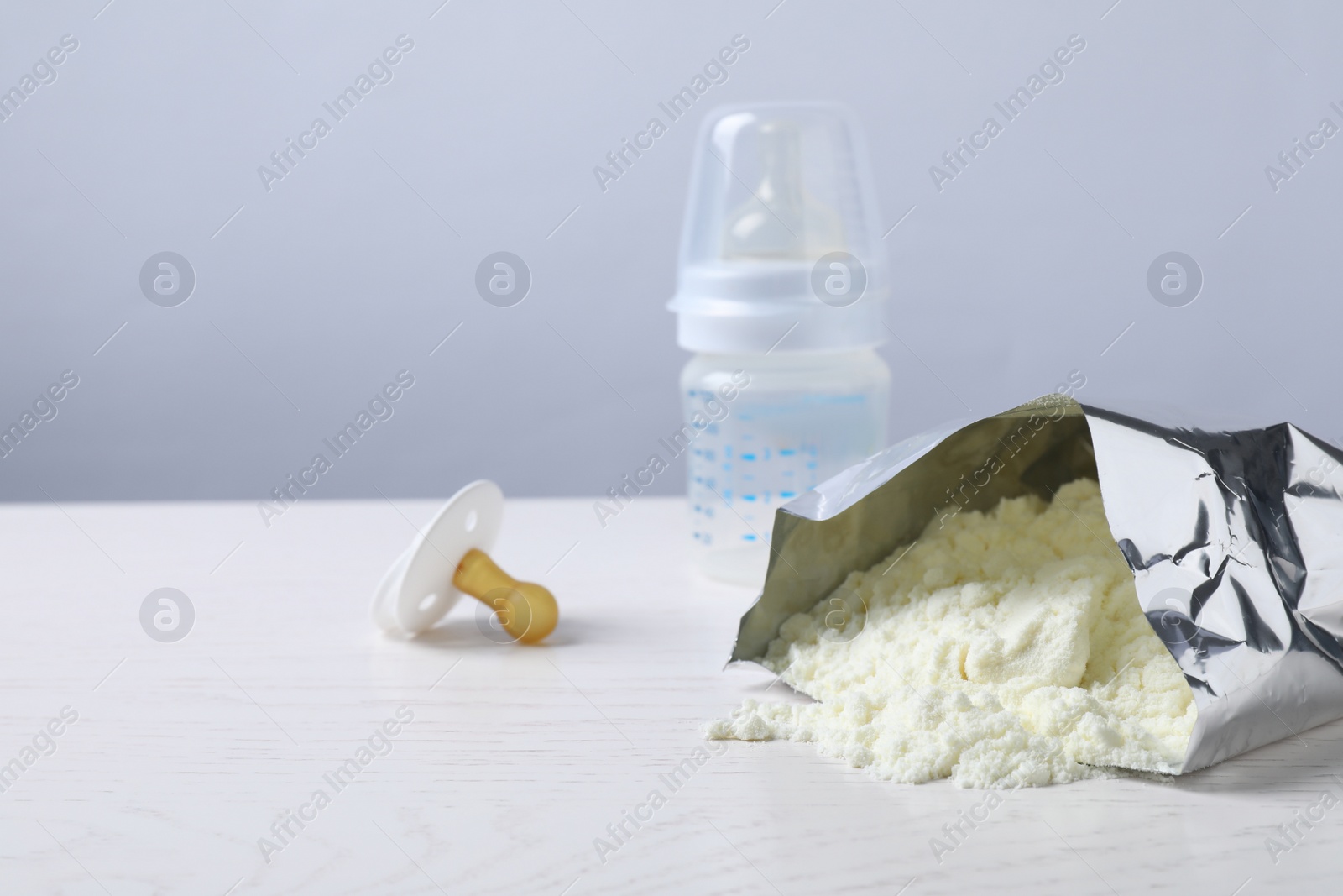 Photo of Bag of powdered infant formula, feeding bottle and pacifier on white wooden table, space for text. Baby milk