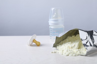 Bag of powdered infant formula, feeding bottle and pacifier on white wooden table, space for text. Baby milk