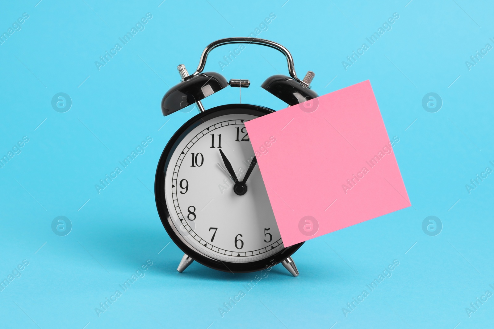 Photo of Alarm clock and blank reminder note on light blue background, space for text