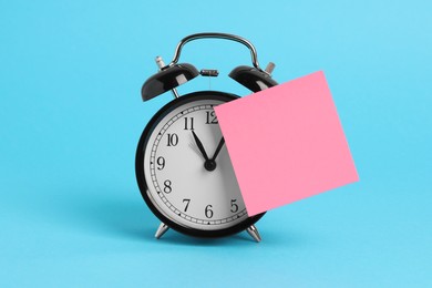 Alarm clock and blank reminder note on light blue background, space for text