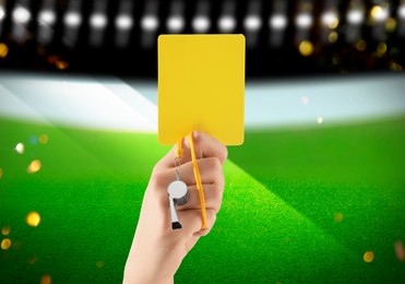 Referee holding yellow card and whistle at stadium, closeup