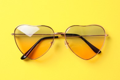 Photo of Stylish elegant heart shaped sunglasses on yellow background, top view
