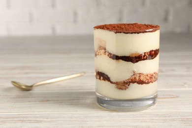 Photo of Delicious tiramisu in glass on light wooden table, closeup. Space for text