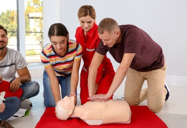 Photo of Group of people with instructor practicing CPR on mannequin at first aid class indoors