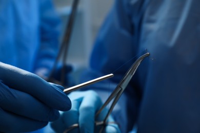 Photo of Professional surgeons with forceps and suture thread on blurred background, closeup. Medical equipment