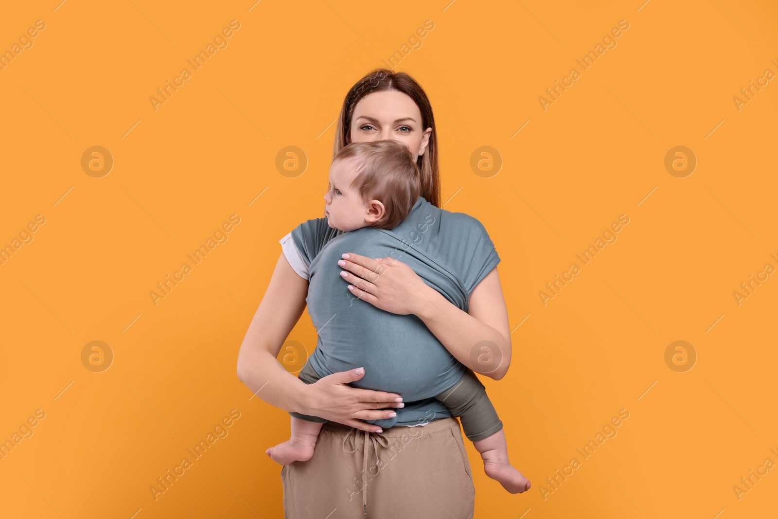 Photo of Mother holding her child in baby wrap on orange background