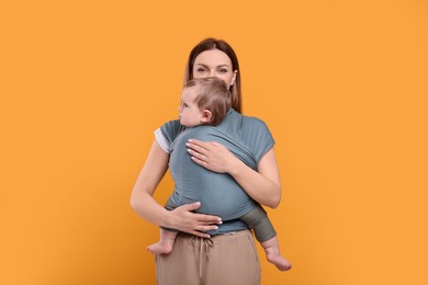 Photo of Mother holding her child in baby wrap on orange background