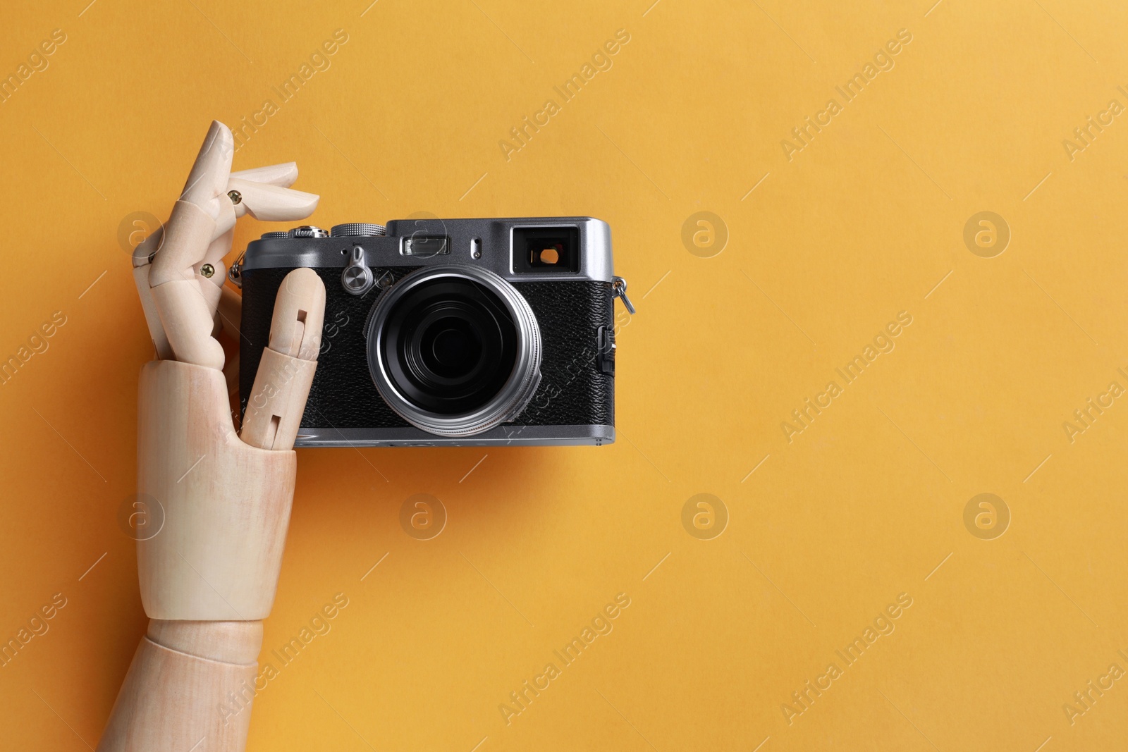 Photo of Wooden mannequin hand with camera on orange background, top view. Space for text