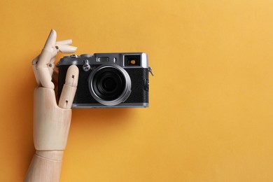 Photo of Wooden mannequin hand with camera on orange background, top view. Space for text