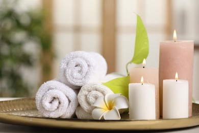 Photo of Spa composition. Burning candles, plumeria flower, green leaves and towels on table indoors