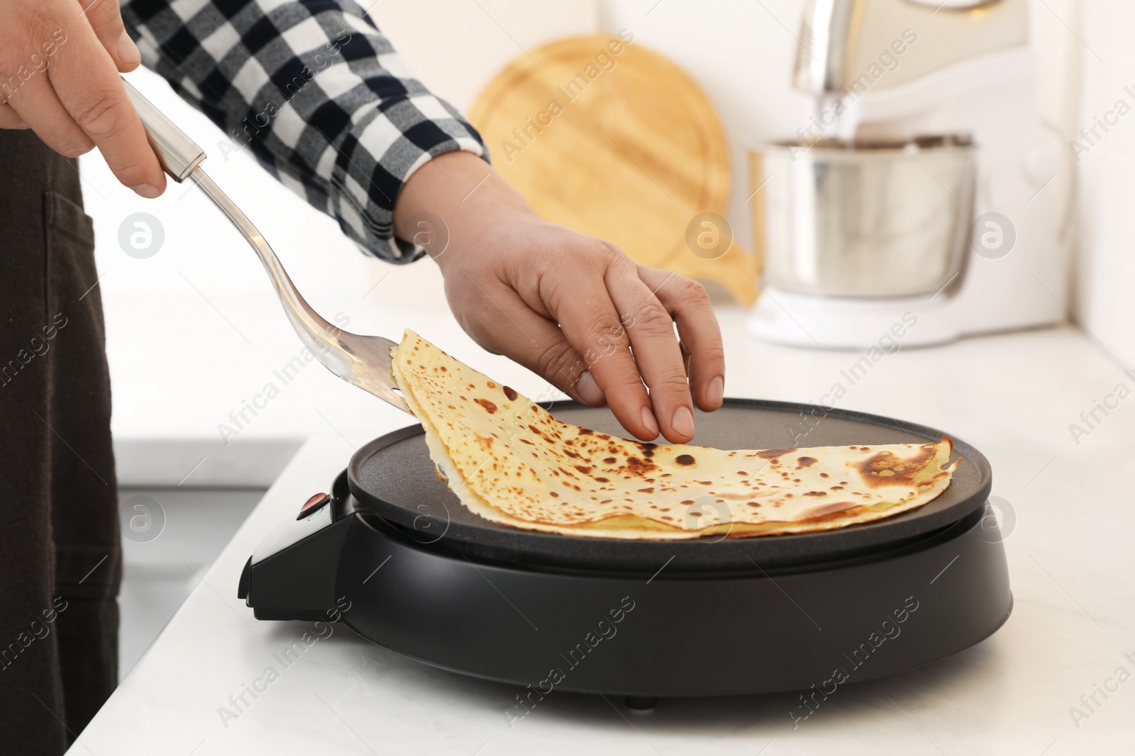 Photo of Man cooking delicious crepe on electric pancake maker in kitchen, closeup