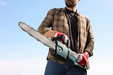 Photo of Man with modern saw against blue sky, closeup