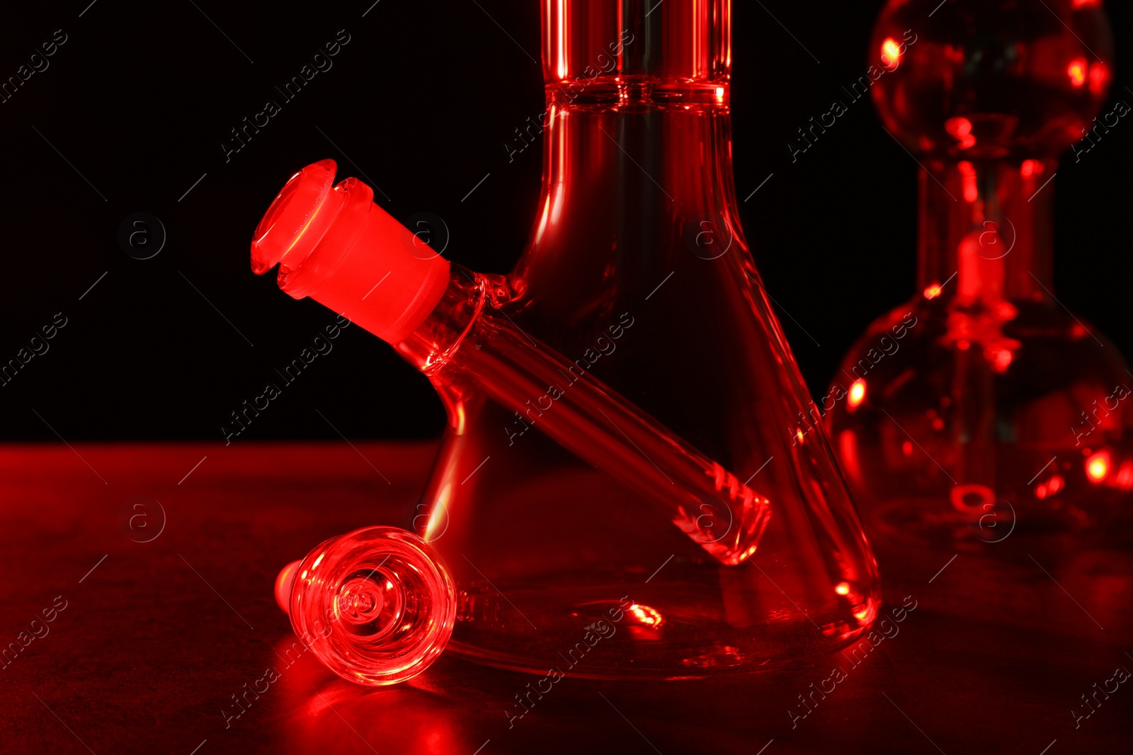Photo of Glass bongs on table against black background, toned in red. Smoking device