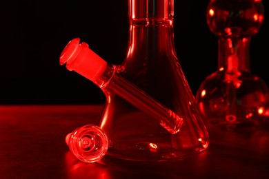 Glass bongs on table against black background, toned in red. Smoking device