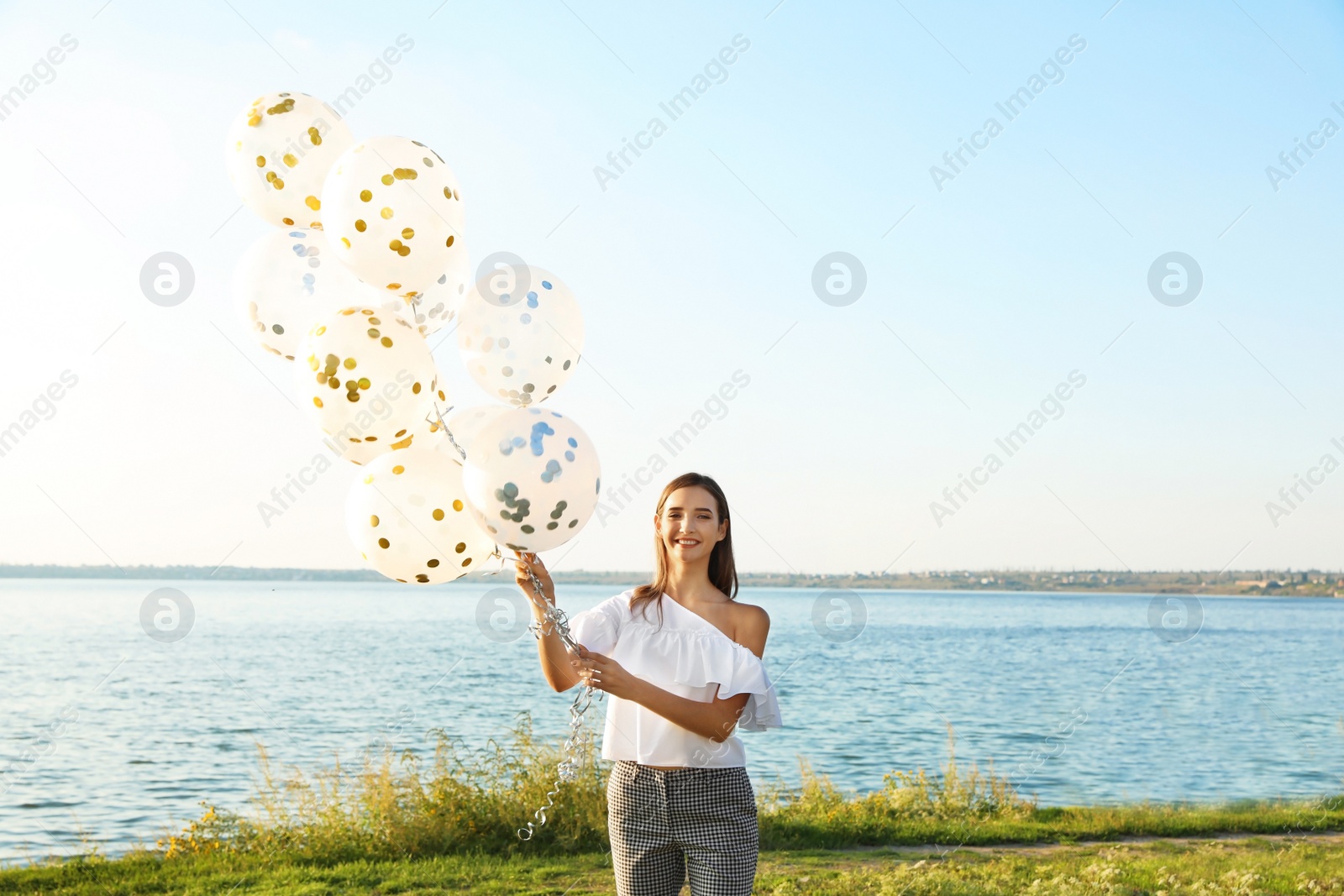 Photo of Beautiful teenage girl holding glitter balloons on riverside