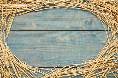 Frame of dried hay on light blue wooden background, flat lay. Space for text