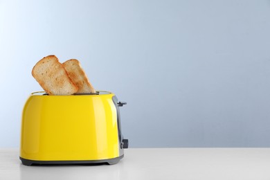 Photo of Bread slices popping up out of electric toaster on light table. Space for text