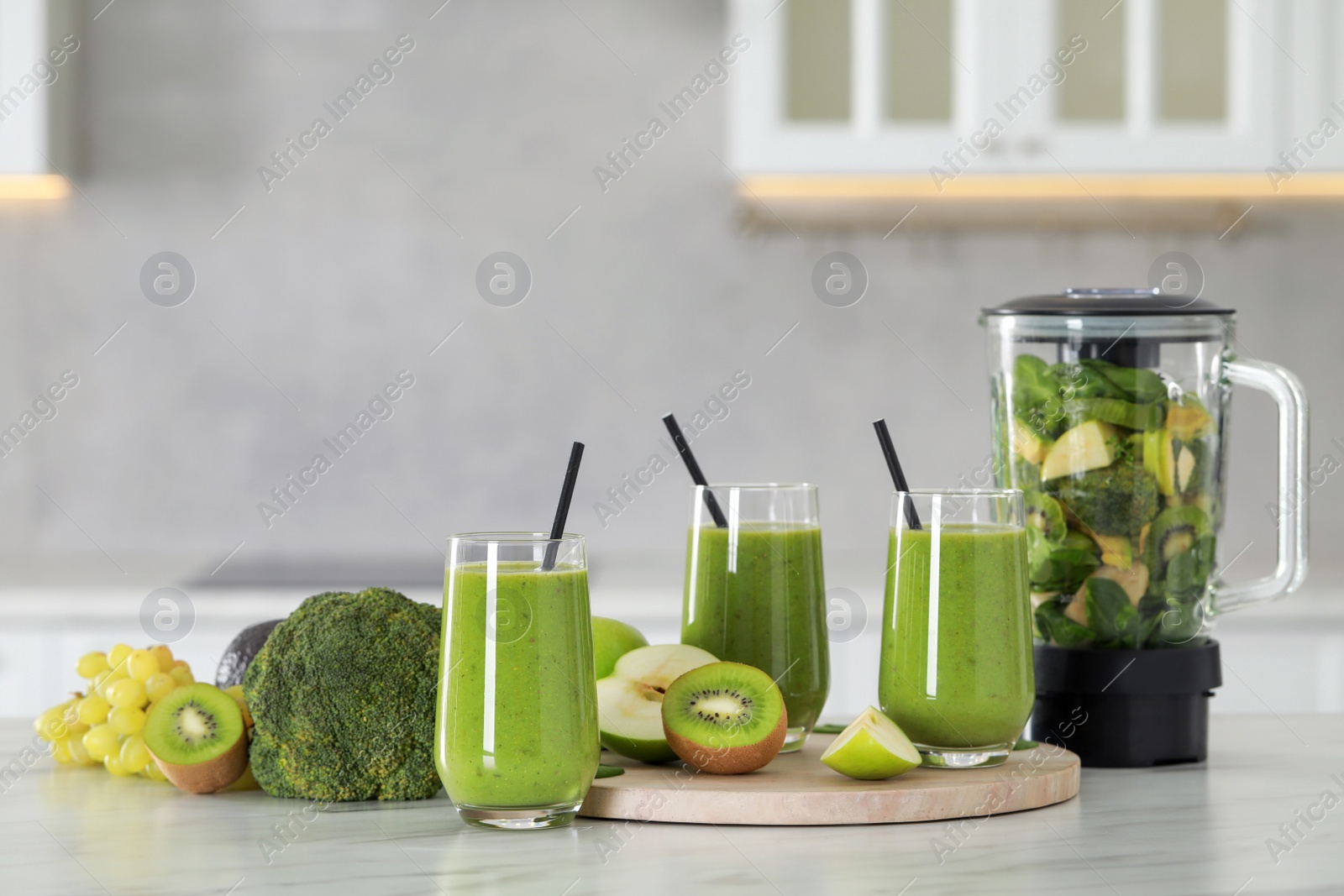 Photo of Delicious fresh smoothie and blender with ingredients on white marble table in kitchen