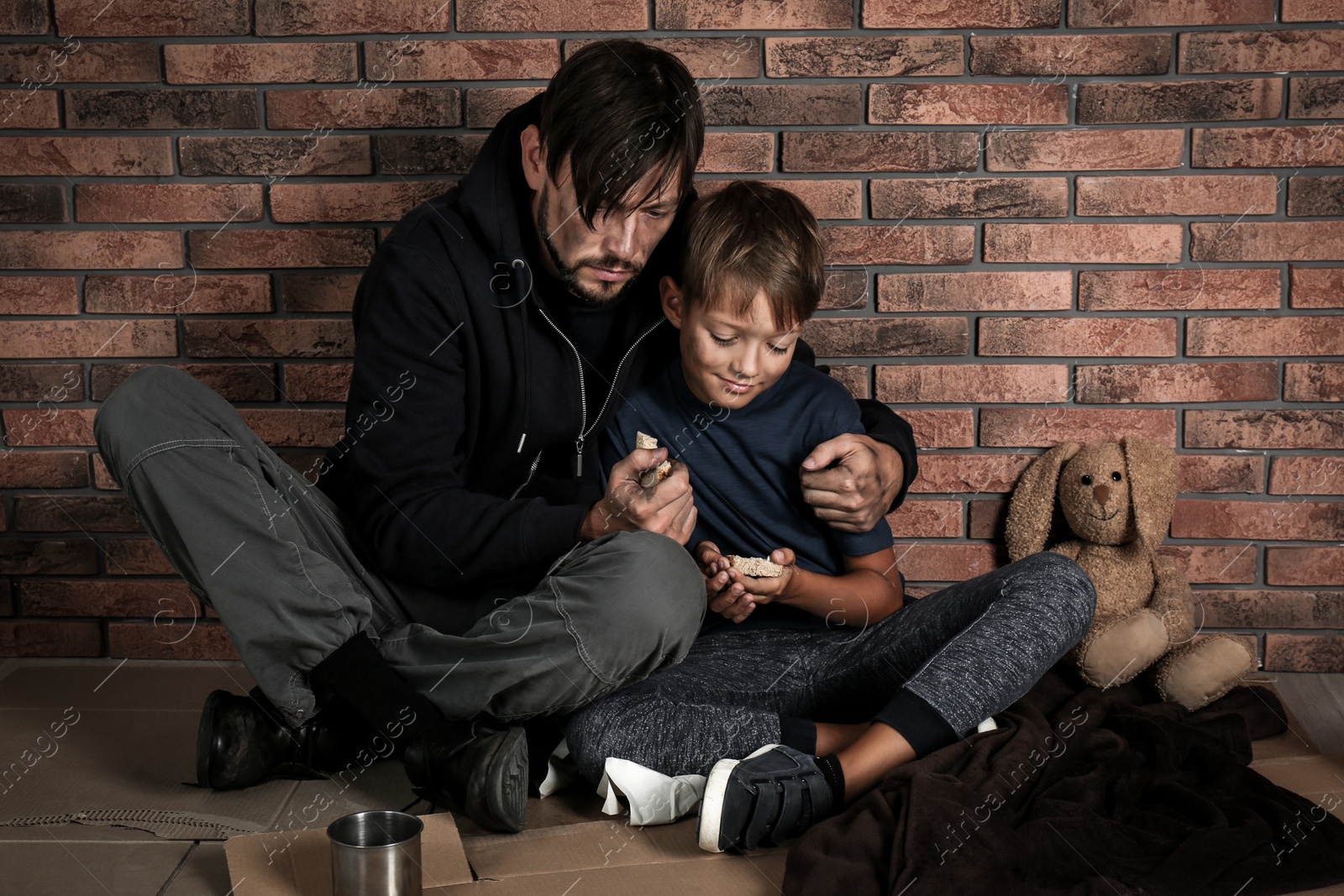 Photo of Poor man and his son sitting om floor near brick wall