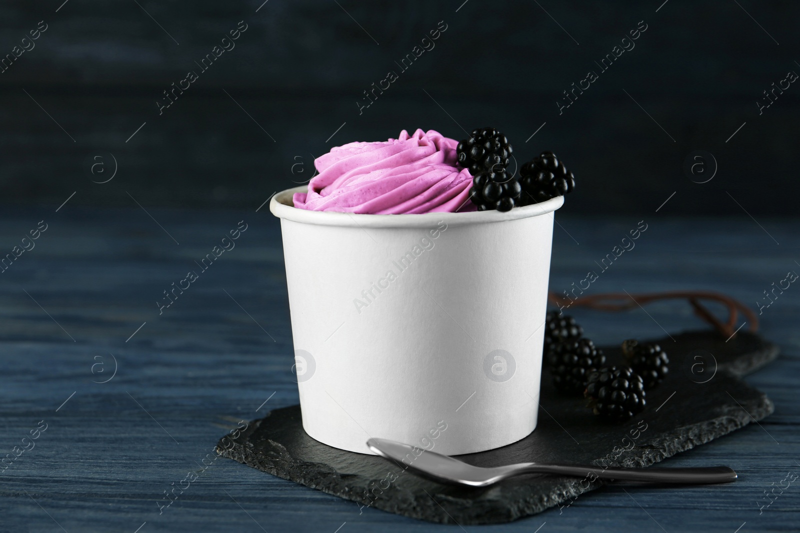 Photo of Cup with tasty frozen yogurt and blackberries on blue wooden table