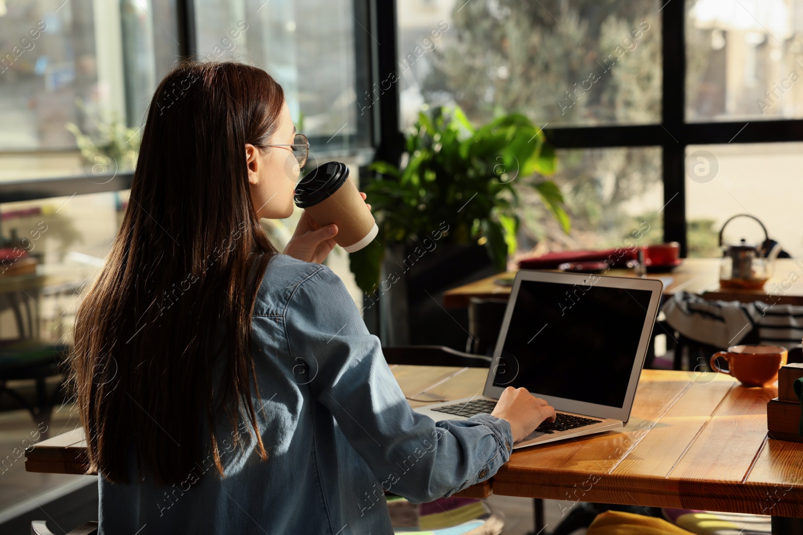 Photo of Young female student with laptop drinking coffee while studying at table in cafe