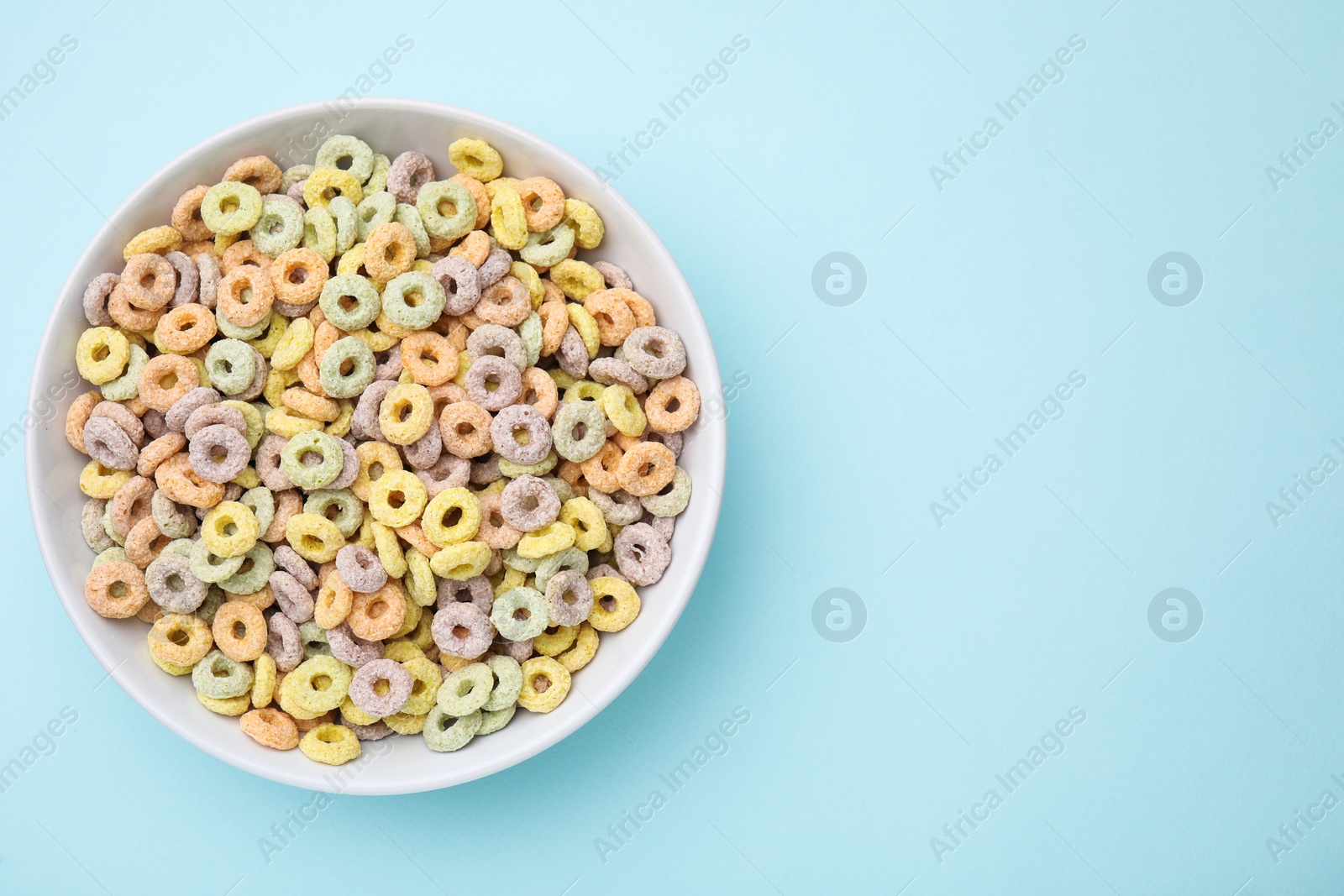 Photo of Tasty cereal rings in bowl on light blue table, top view. Space for text