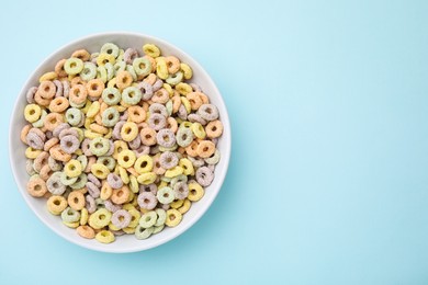 Photo of Tasty cereal rings in bowl on light blue table, top view. Space for text