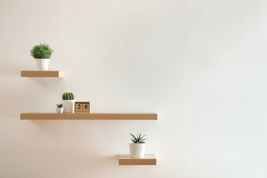 Photo of Wooden shelves with beautiful plants and calendar on light wall