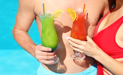 Photo of Young couple with refreshing cocktails near swimming pool at resort