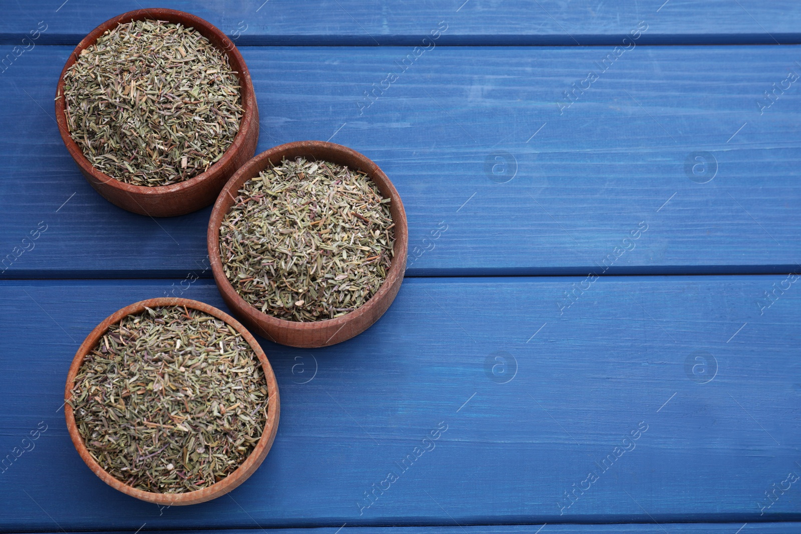 Photo of Bowls with dried thyme on blue wooden table, flat lay. Space for text