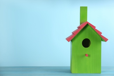 Beautiful bird house on wooden table against light blue background, space for text