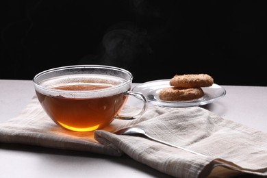Photo of Glass cup of tea with cookies on table against black background