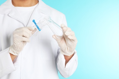 Photo of Male doctor holding disposable speculum on color background, closeup with space for text. Medical object