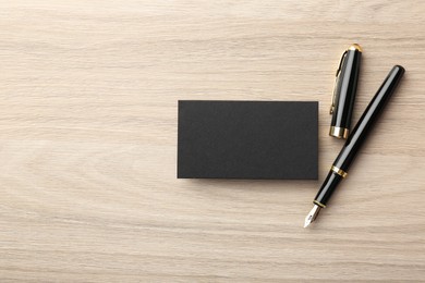 Photo of Blank black business card and fountain pen on wooden table, flat lay. Mockup for design