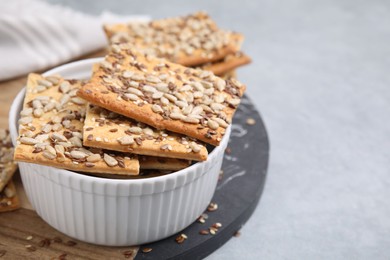 Photo of Cereal crackers with flax, sunflower and sesame seeds in bowl on grey table, closeup. Space for text