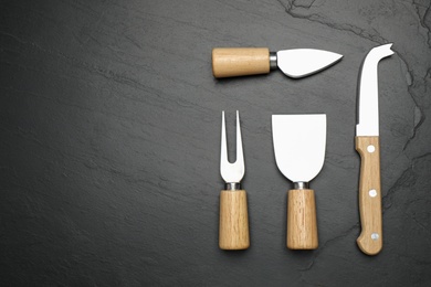 Photo of Cheese knives and fork on black stone table, flat lay