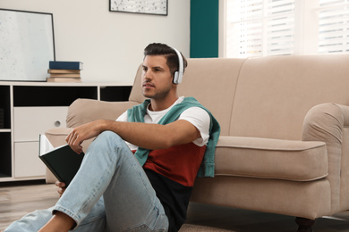 Man with headphones and book near sofa indoors. Audiobook concept