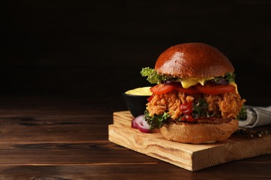 Photo of Delicious burger with crispy chicken patty on wooden table. Space for text