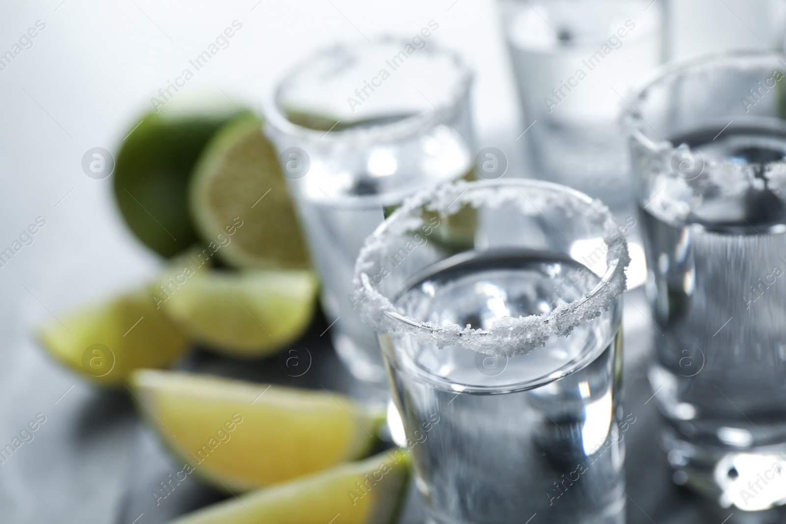 Photo of Mexican Tequila shots, lime slices and salt on grey table, closeup