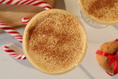 Photo of Tasty eggnog with cinnamon, cookies and candy canes on white table, flat lay