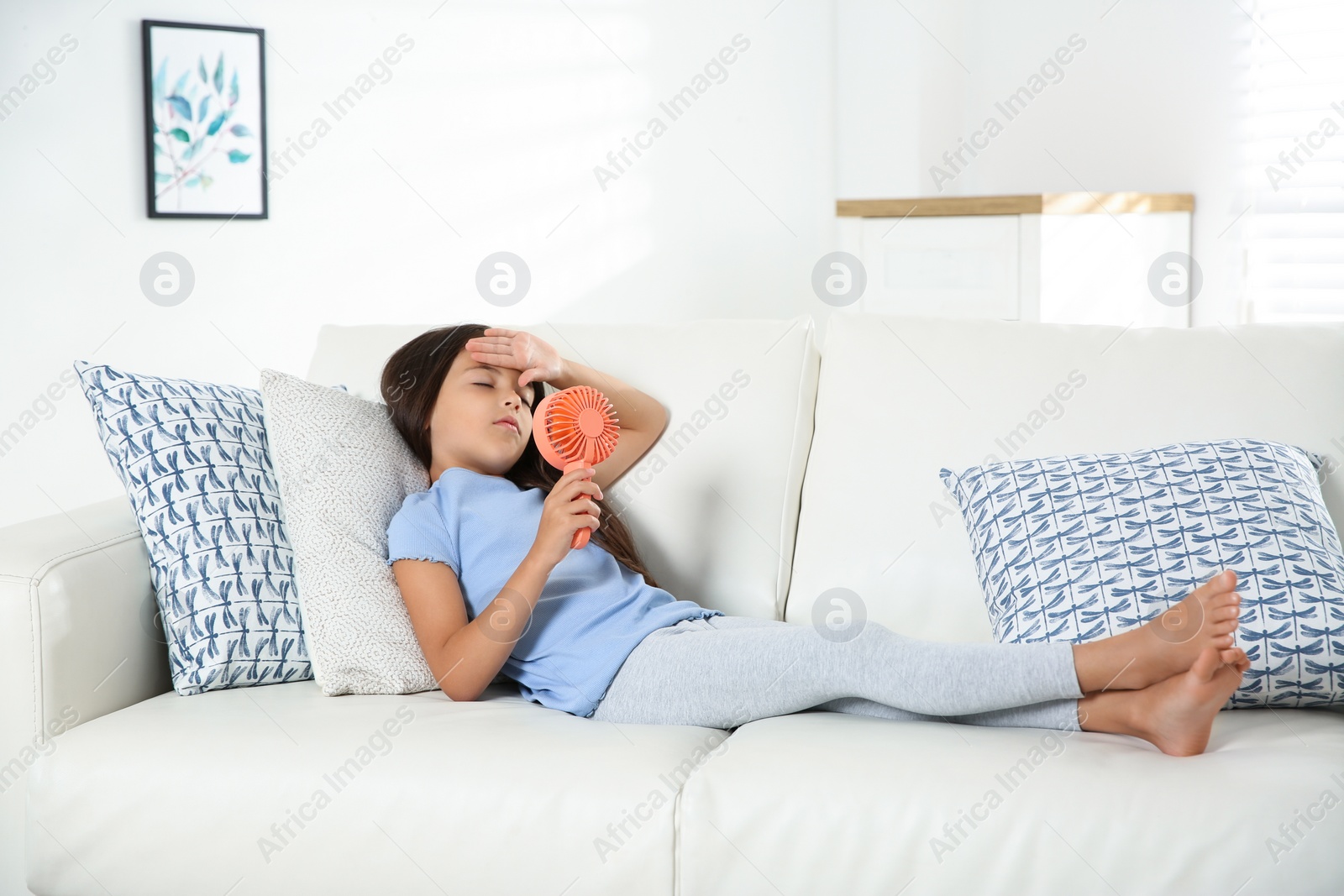 Photo of Little girl with portable fan suffering from heat at home. Summer season