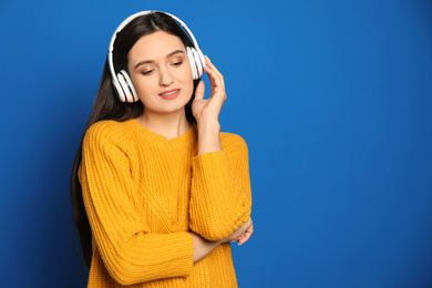 Young woman listening to audiobook on blue background. Space for text