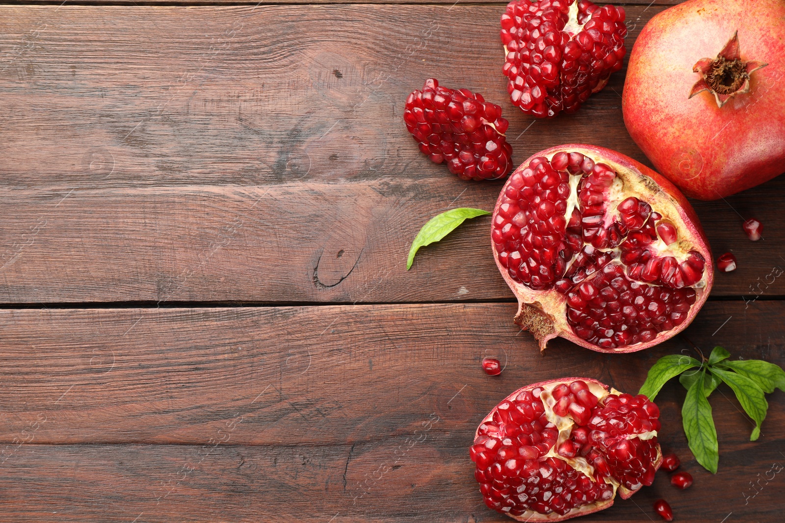 Photo of Fresh pomegranates and green leaves on wooden table, flat lay. Space for text