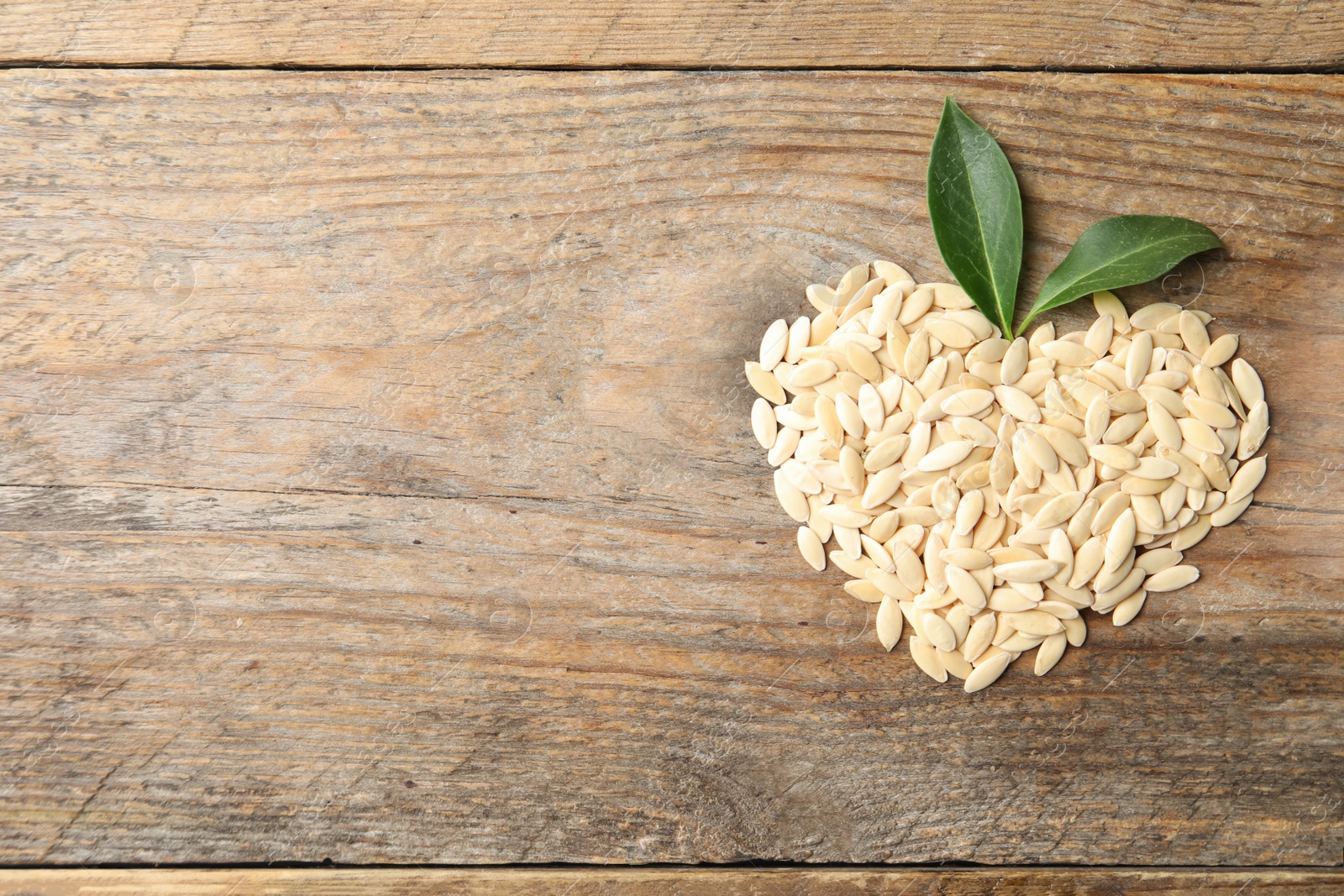 Photo of Heart made of raw cucumber seeds and space for text on wooden background, top view. Vegetable planting