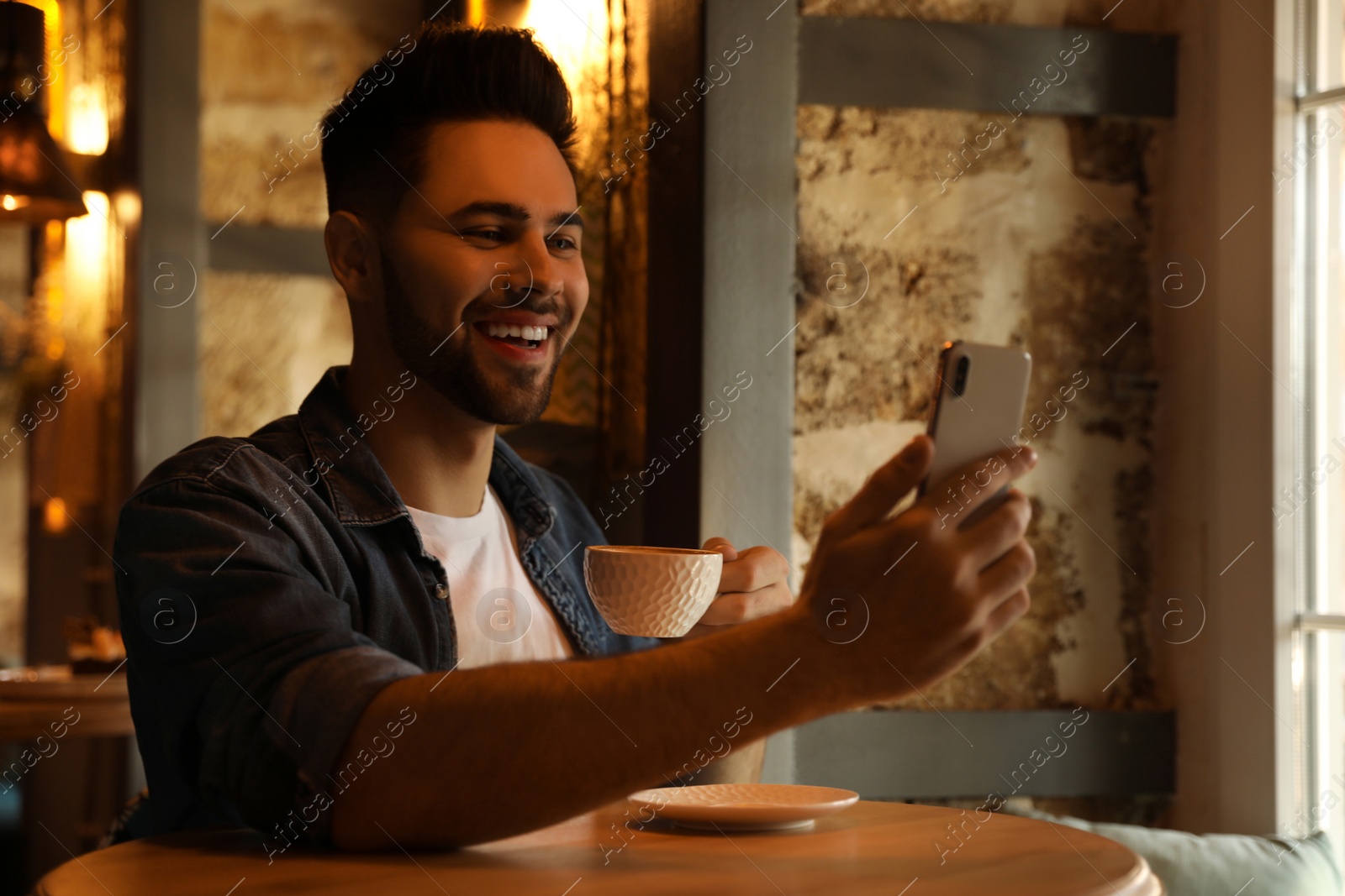 Photo of Young blogger taking selfie at table in cafe