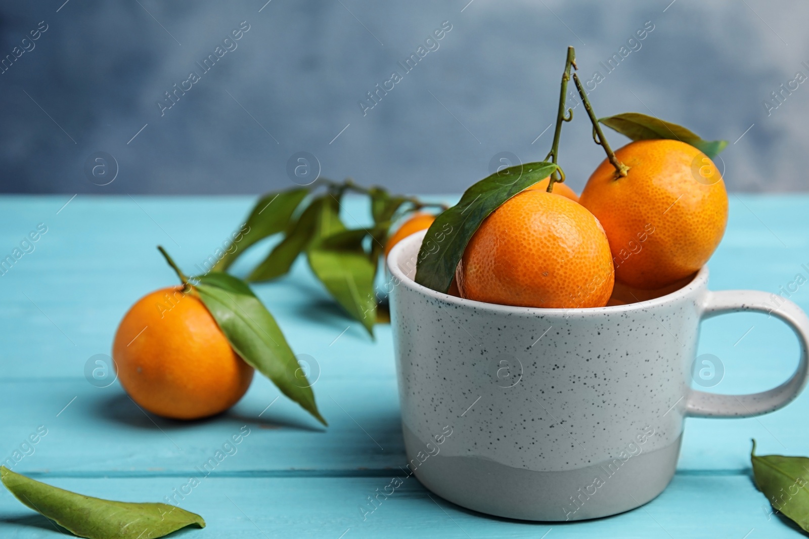 Photo of Fresh ripe tangerines with green leaves and mug on table. Space for text