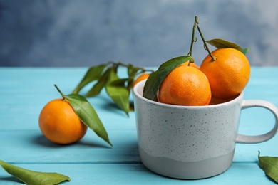 Fresh ripe tangerines with green leaves and mug on table. Space for text